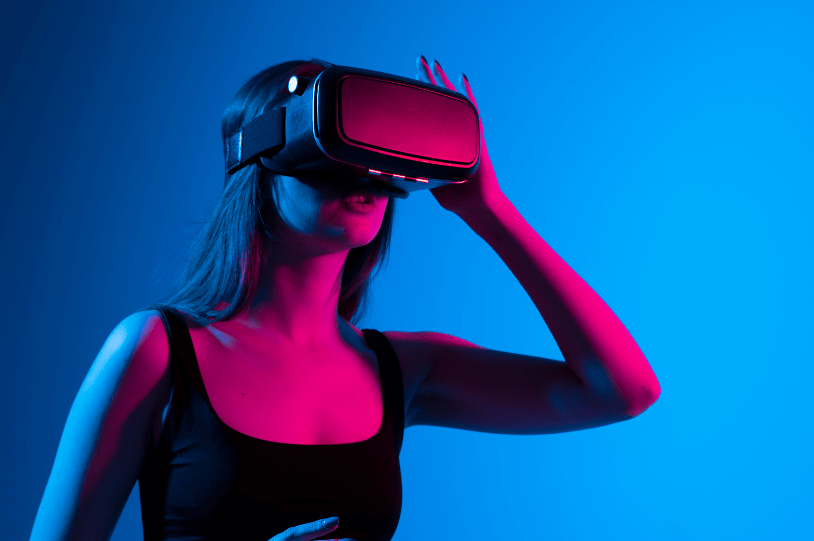 Cheerful girl with hands up wearing virtual reality goggles playing games on Metaverse to get the enhanced VIP experience utilised by luxury brands.